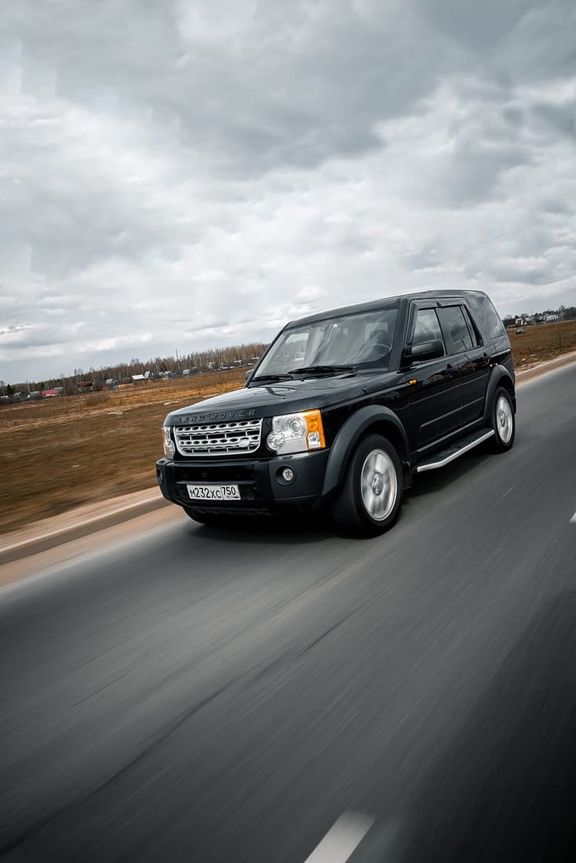 Black Land Rover Discovery SUV driving on an asphalt road under a dark, cloudy sky with visible motion blur.