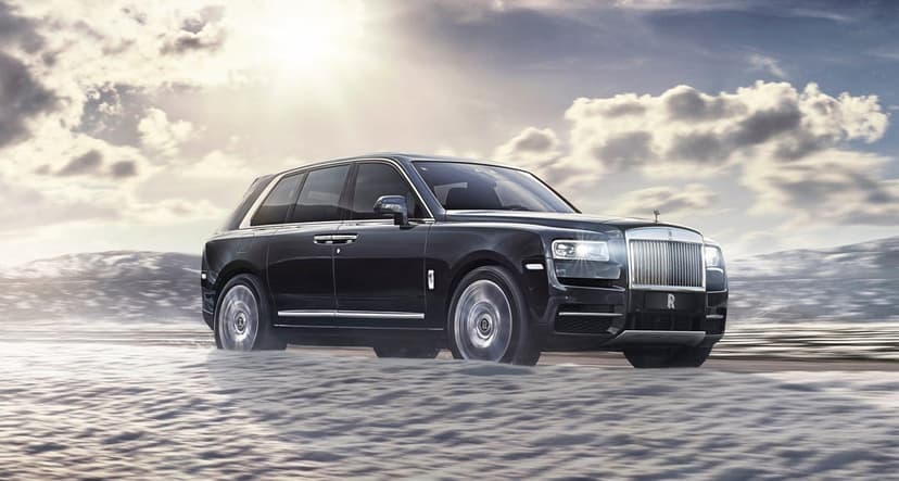 Black luxury SUV driving across white snow under a bright sun with dramatic clouds in a landscape view.