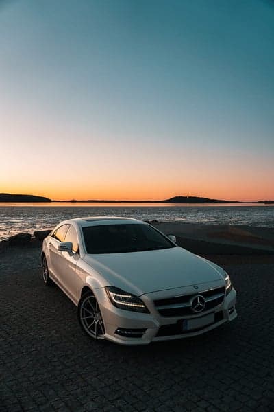 White Mercedes CLS parked by the sea at sunset