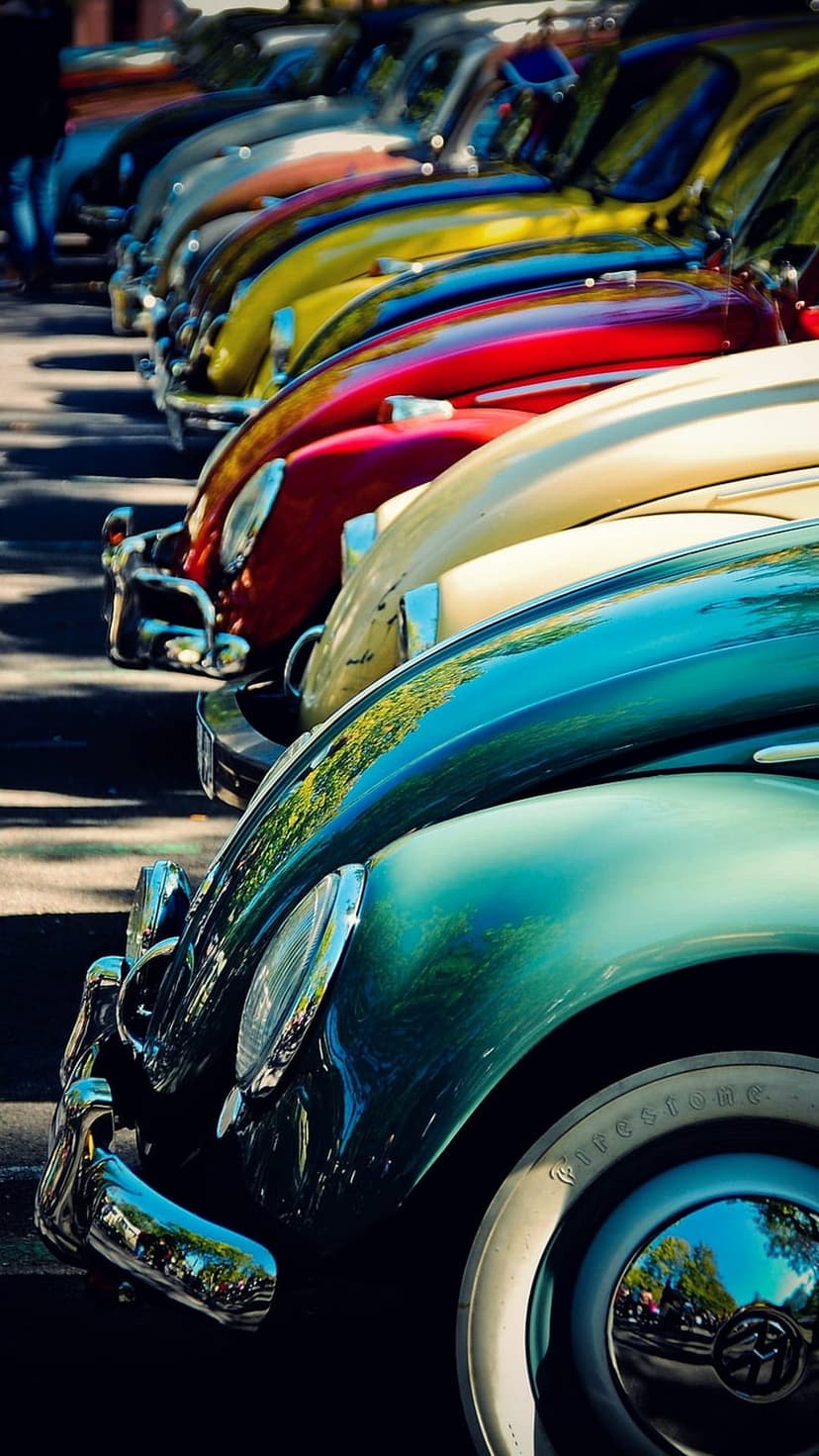 Classic Volkswagen Beetles in teal, red, and yellow park diagonally, showcasing chrome bumpers and round curves.