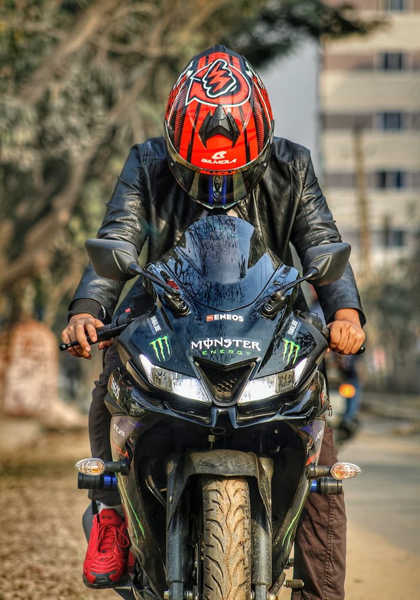 Motorcyclist in a red helmet and black jacket leans over a bike with Monster Energy decals on the handlebars.