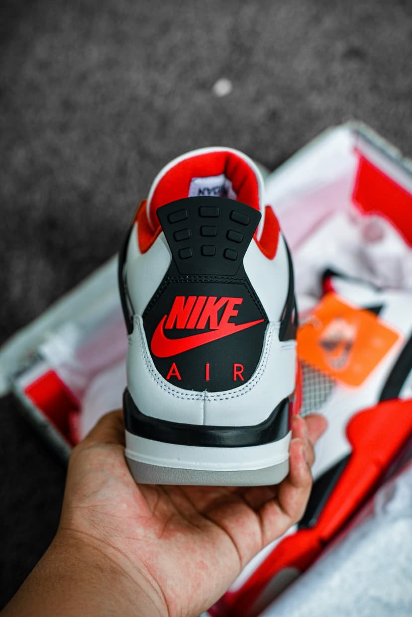 Nike Air Jordan 4 heel with a red logo and black accents against a blurred shoebox background in a vertical shot.