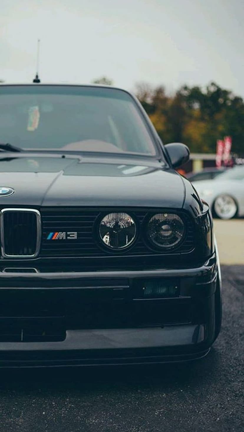 BMW E30 M3 front fascia with dual round headlights and an M-badged grille against a blurred background.