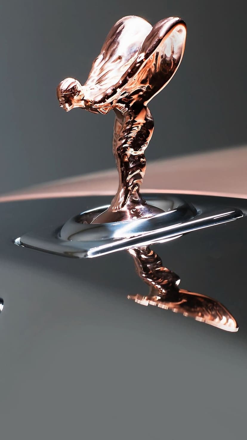 Spirit of Ecstasy sculpture in polished copper with flowing robes and wings against a soft grey background.