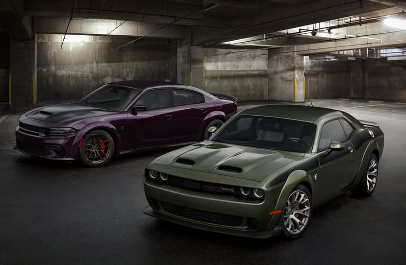 Green Dodge Challenger and purple Dodge Charger parked in a dark concrete garage with soft overhead lighting.