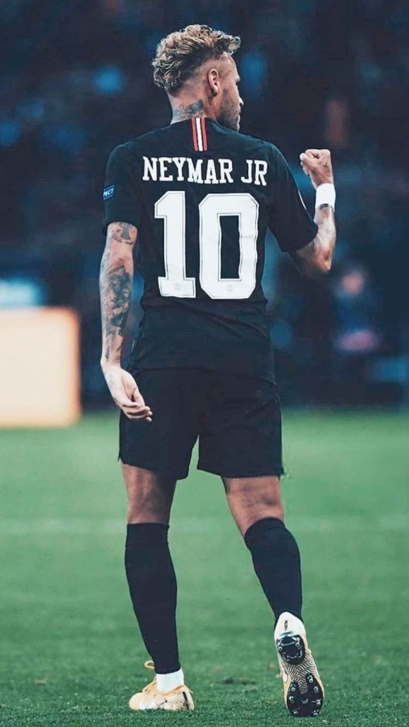 Neymar Jr. raises his fist in a black number 10 jersey while standing on a green grass soccer pitch.