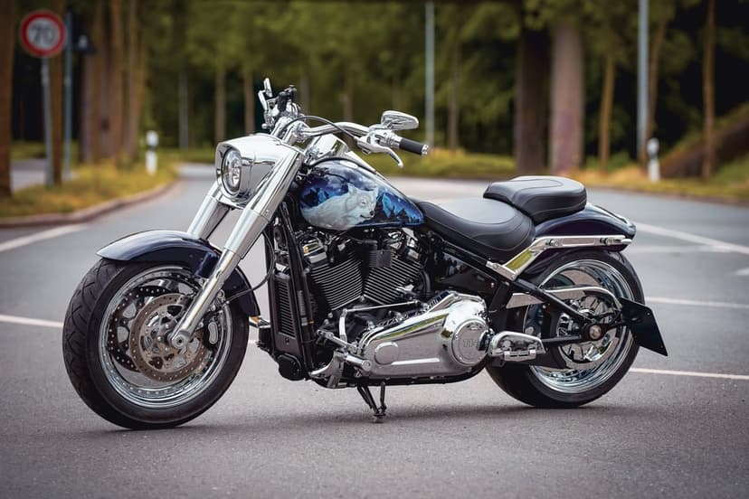 Custom cruiser motorcycle with a white wolf painted on the tank and chrome wheels on a paved forest road.