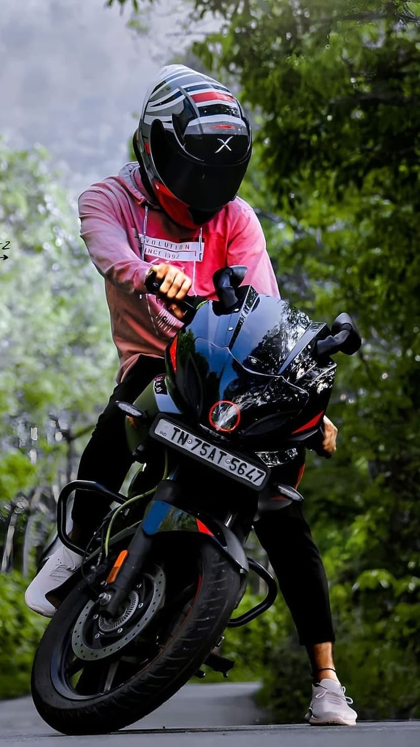 Rider wearing a pink hoodie and black helmet on a sports motorcycle surrounded by lush green forest trees.