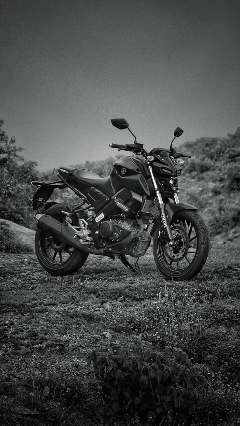 Black Yamaha motorcycle parked on a grassy hillside in a side-profile view with a monochrome photography style.