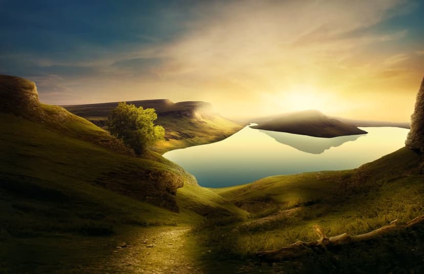 Rolling green hills surround a calm lake reflecting orange sunset light with a winding path in the foreground.