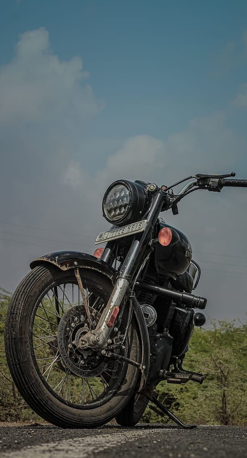 Black Royal Enfield motorcycle featuring a round LED headlight and orange turn signals parked on an asphalt road.