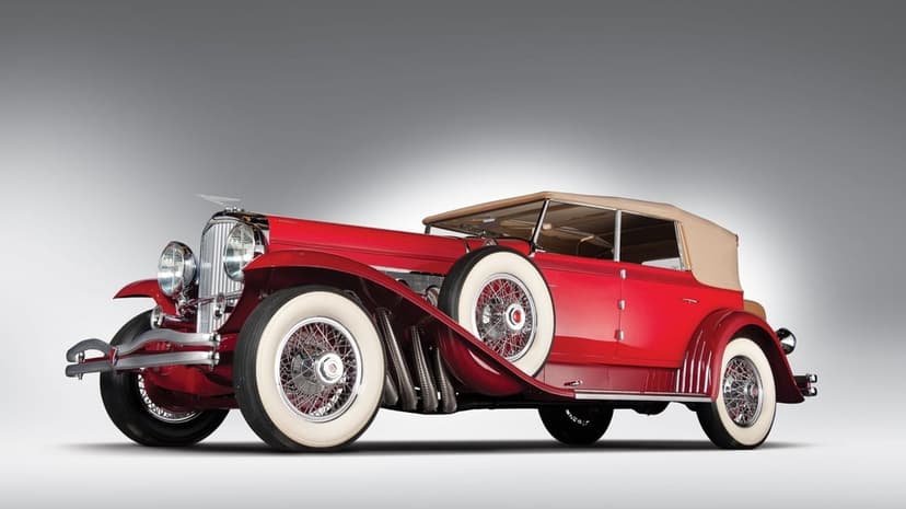 Red classic car with chrome details, tan top, and white-wall tires against a grey studio backdrop.