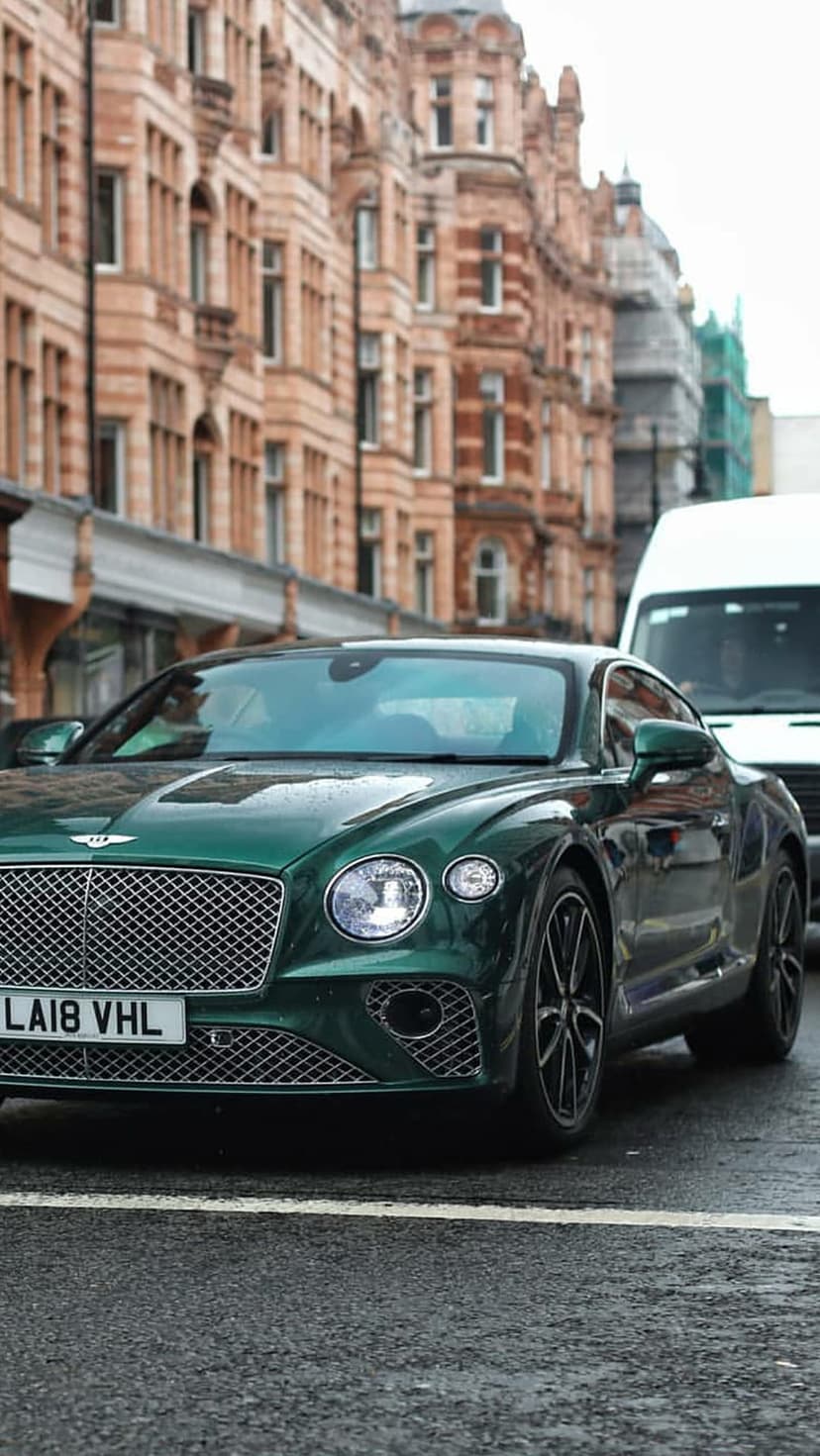 Bentley Continental GT in dark green parked on a damp cobbled street with historic London brick buildings.