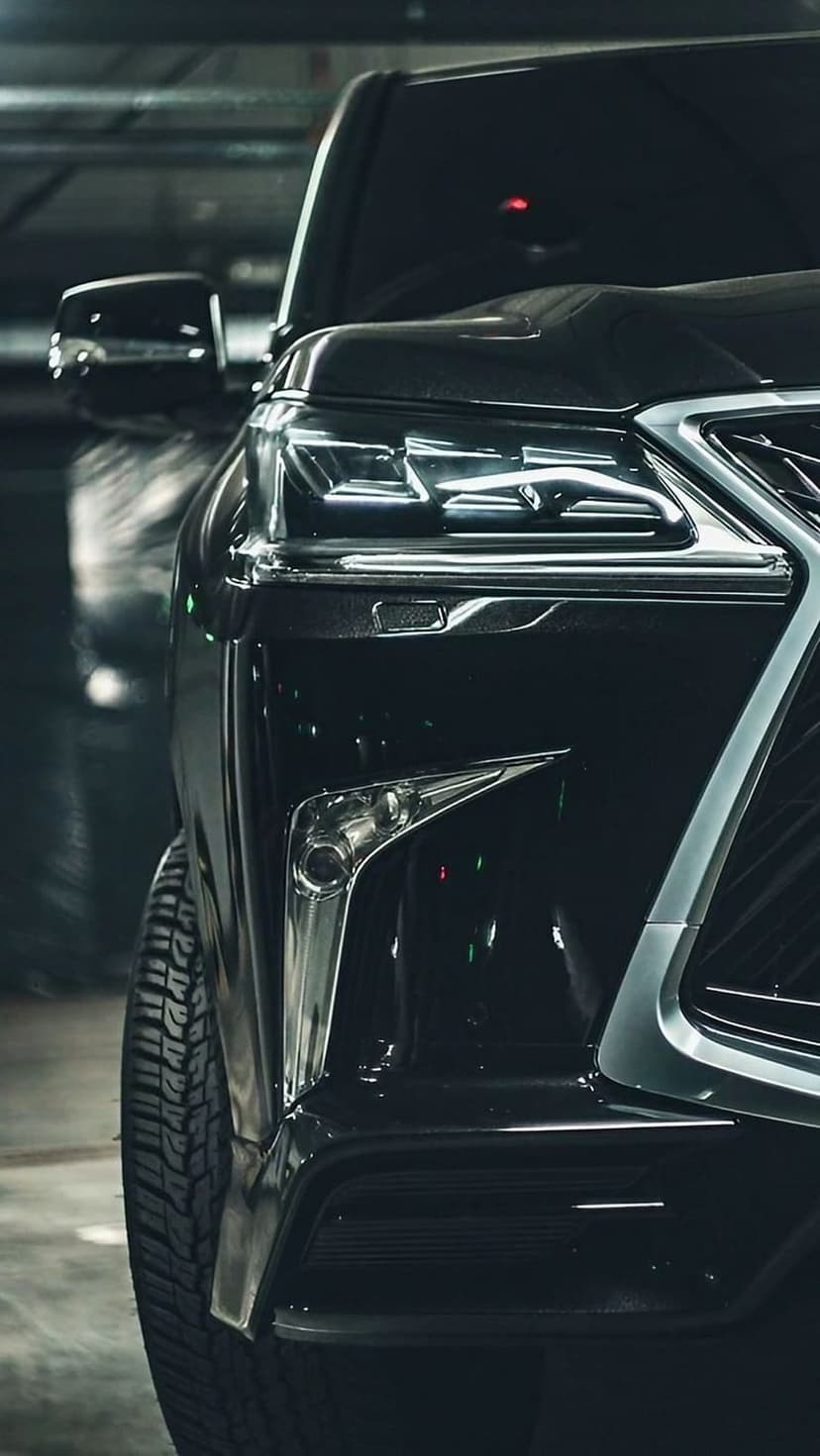 Lexus SUV front grille and sharp LED headlight with a glossy black finish against a dark textured background.