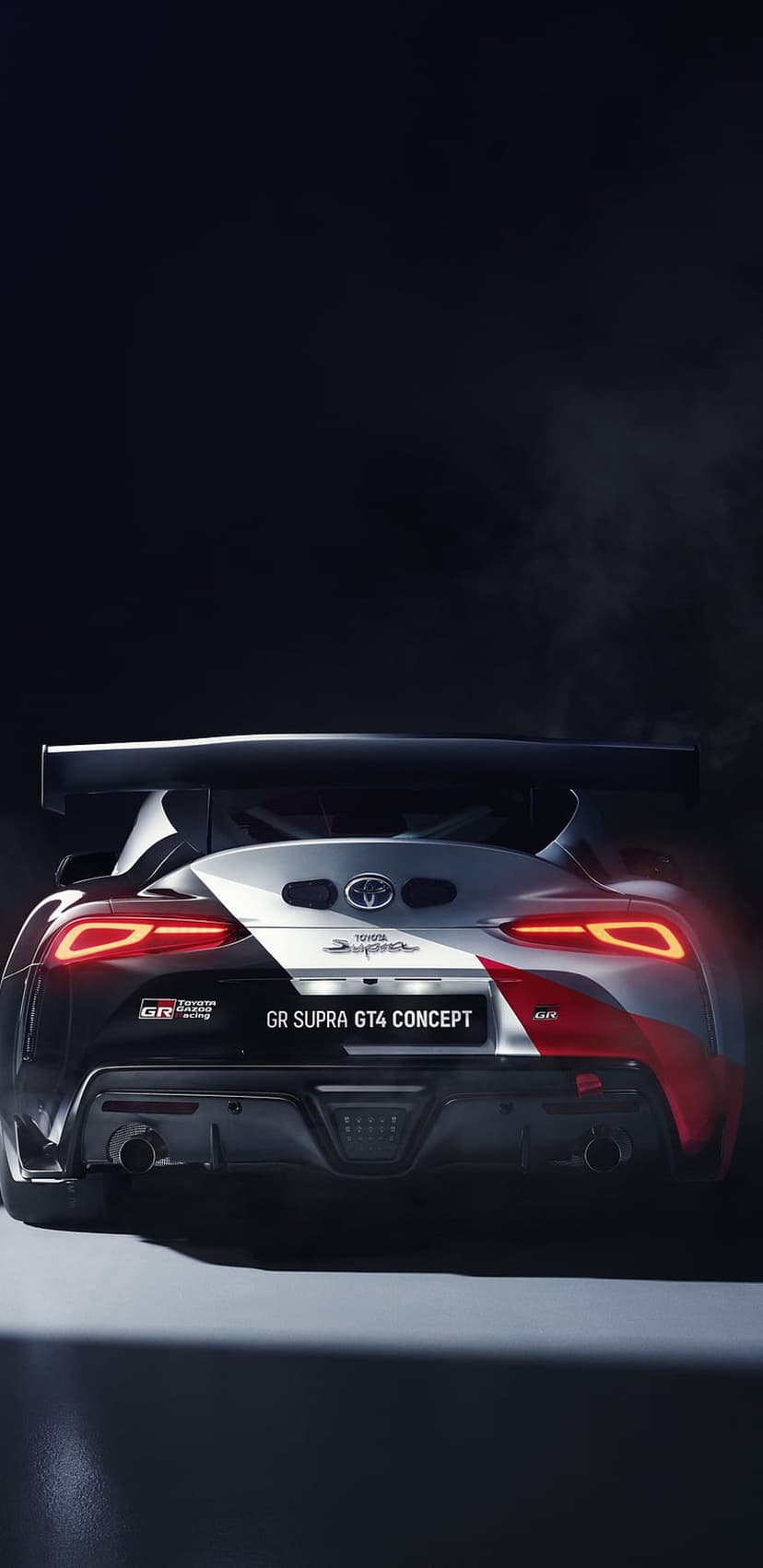 Toyota GR Supra GT4 Concept rear view featuring a large racing wing, red taillights, and dual exhaust tips.