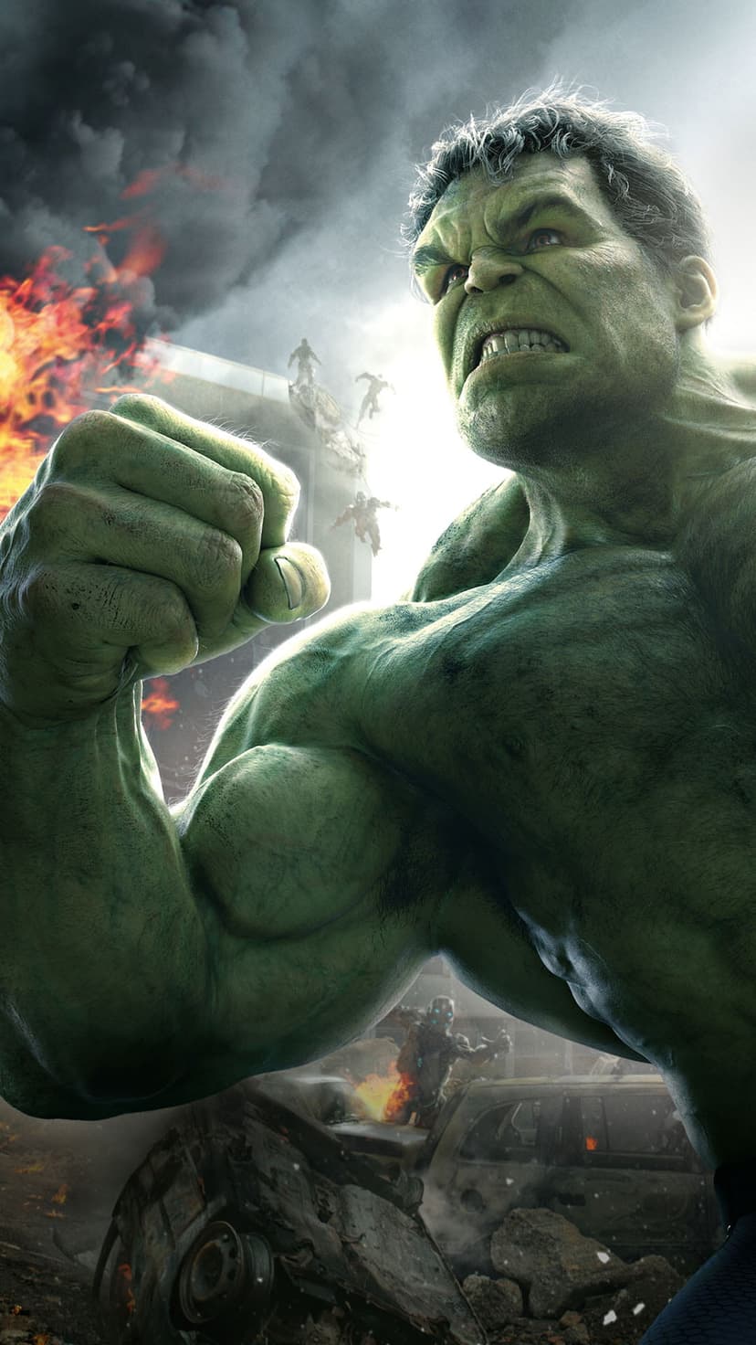 Hulk roars while crashing through a burning city street filled with flipped cars and rising black smoke.