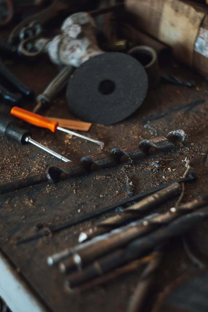 Black circular grinder disc lies amidst orange-handled screwdrivers and drill bits on a messy wooden workbench.