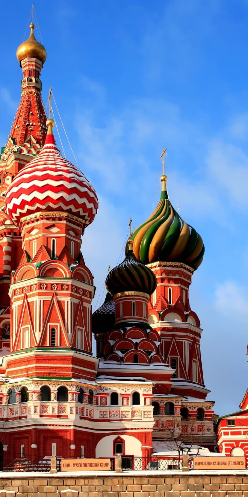 Saint Basil’s Cathedral displays colorful onion domes and red brickwork against a bright blue sky with clouds.