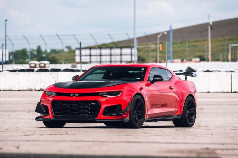 Red Chevrolet Camaro ZL1 with black aero parts and spoiler parked on a concrete racetrack under daylight.