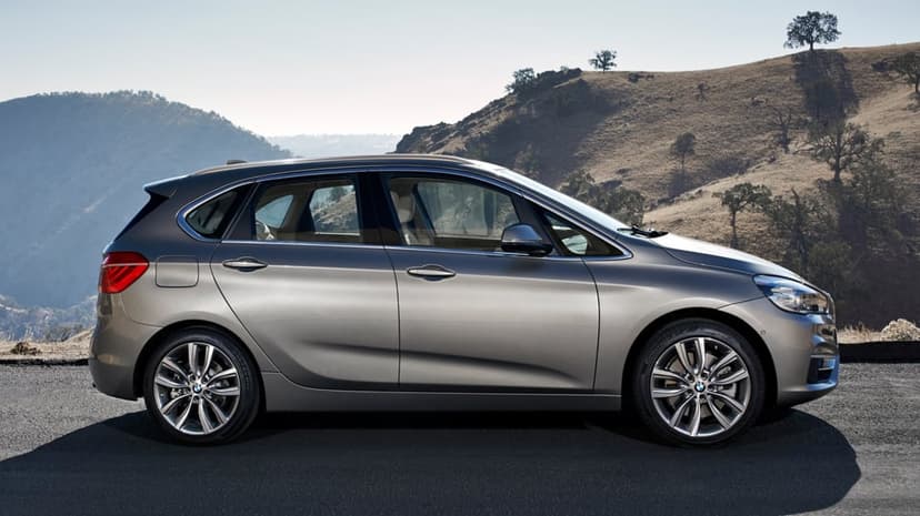 Silver BMW hatchback parked on an asphalt road with dry, rolling hills and scattered trees in the background.