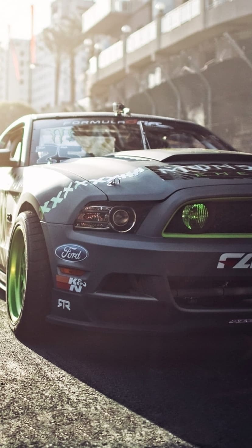 Ford Mustang drift car with matte black paint and neon green wheels parked at a low angle in bright sunlight.