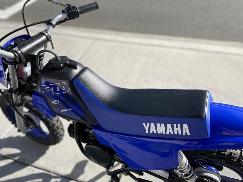 Side view of a vibrant blue Yamaha PW50 dirt bike seat and fuel tank sitting on sunny concrete pavement.