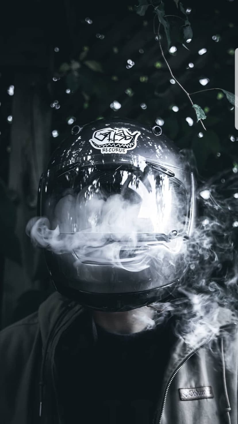 Motorcycle helmet with smoke pouring from the visor against a dark background with blurred bokeh lights.