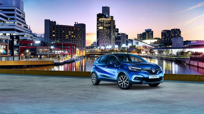 Blue Renault Captur parked on a waterfront platform with a glowing city skyline and sunset reflections.