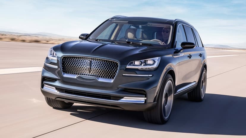Dark Lincoln Aviator SUV driving on a sunlit desert road with motion blurred wheels and a clear blue sky.