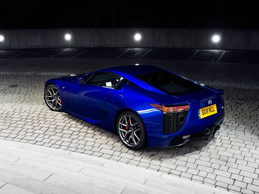 Deep blue Lexus LFA parked on cobblestones at night under spotlights featuring its iconic triple exhaust system.