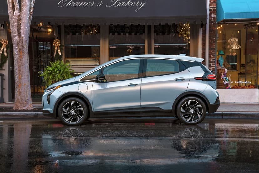Profile of a silver electric hatchback parked on a wet city street with bakery window reflections.