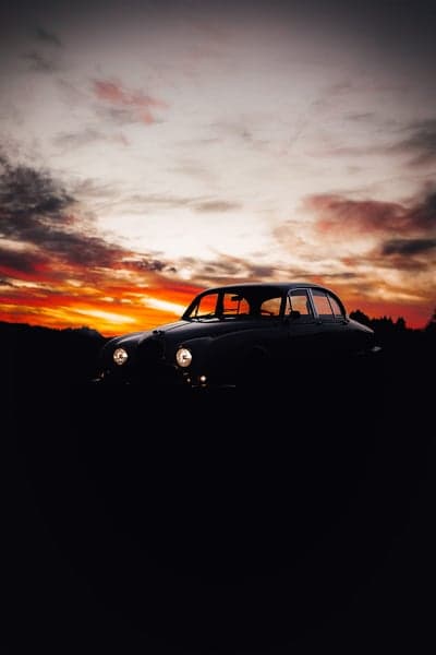 Vintage Jaguar silhouetted against dramatic sunset sky