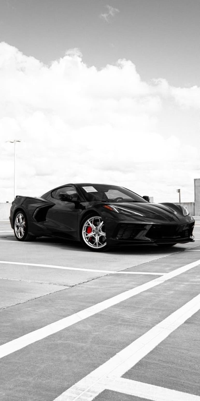 Black Corvette C8 parked on concrete under wispy clouds, featuring red brake calipers and a monochromatic finish.
