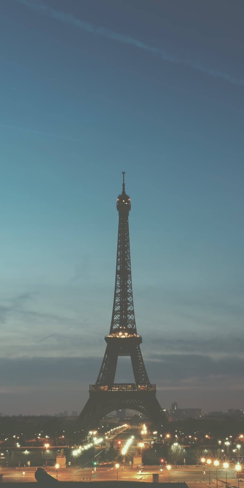 Eiffel Tower glows with warm golden light above a sprawling nocturnal city under a purple and blue twilight sky.