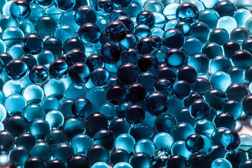 Spherical blue and teal gel beads reflect soft light in a macro close-up, creating a dense, layered texture.