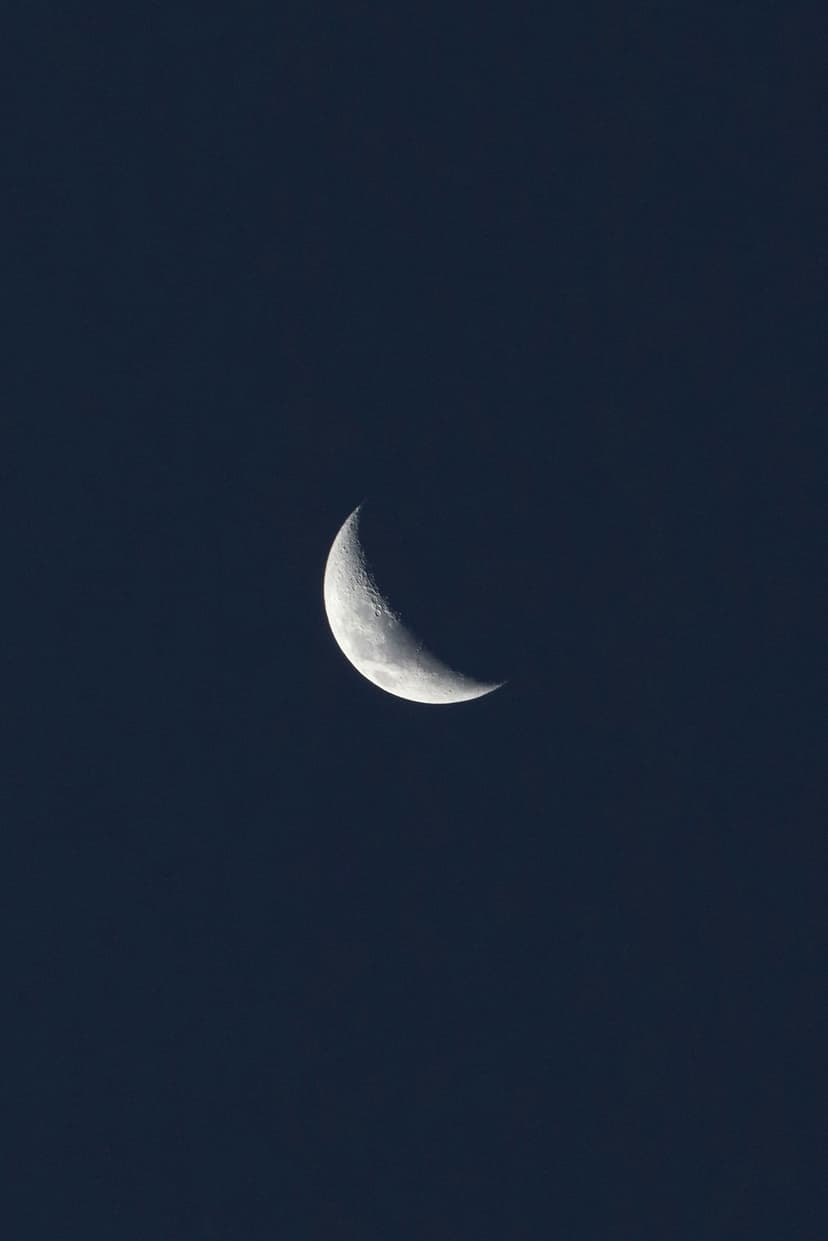 Waxing crescent moon with visible craters shines against a dark navy gradient sky in a vertical composition.