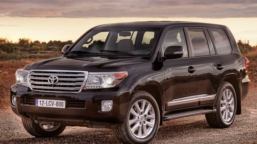 Black Toyota Land Cruiser parked on a dirt path under a sunset sky with orange clouds and chrome accents.