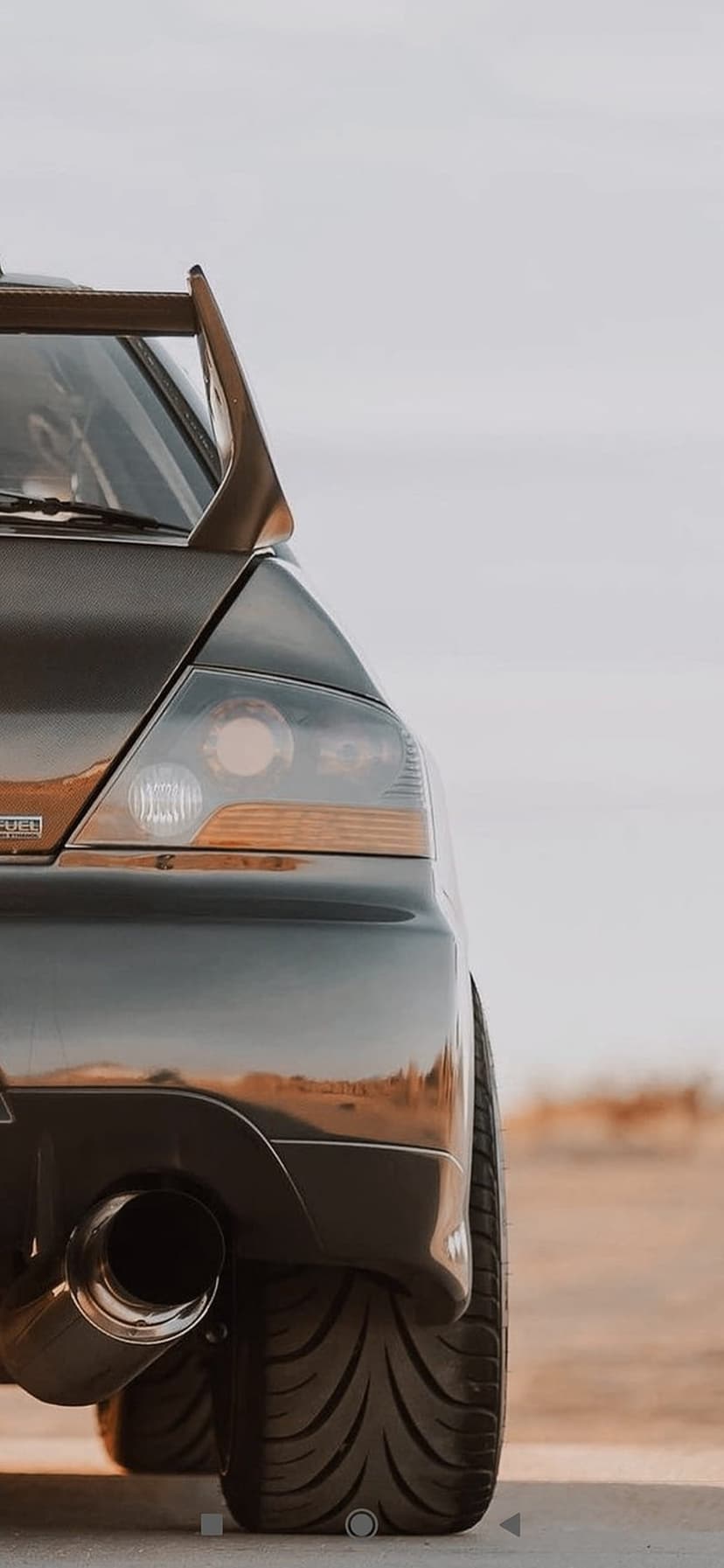 Dark sports car rear with large wing, LED taillights, and wide tires against a blurred desert background.