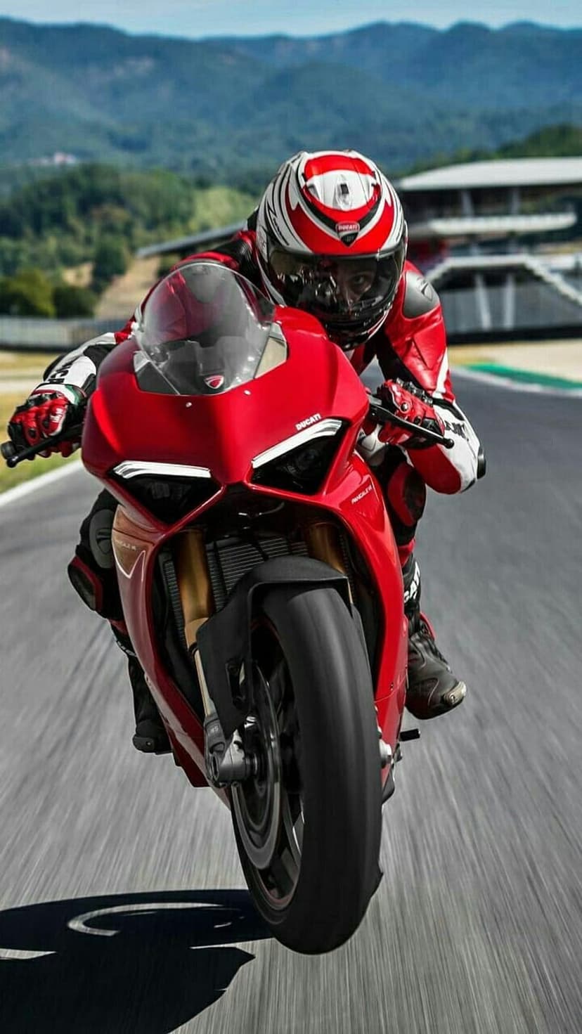 Red Ducati motorcycle rider leans low during a turn on a paved racetrack with motion-blurred scenery.