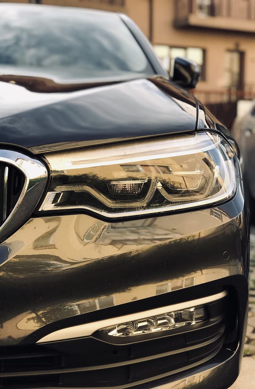 Black luxury car headlight with intricate LED optics and chrome housing reflected on polished dark paint.