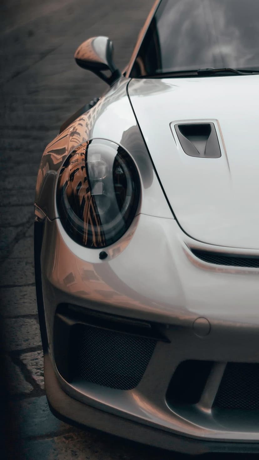 Porsche 911 GT3 silver headlight and hood showing metallic reflections, aerodynamic vents, and sleek car bodywork.
