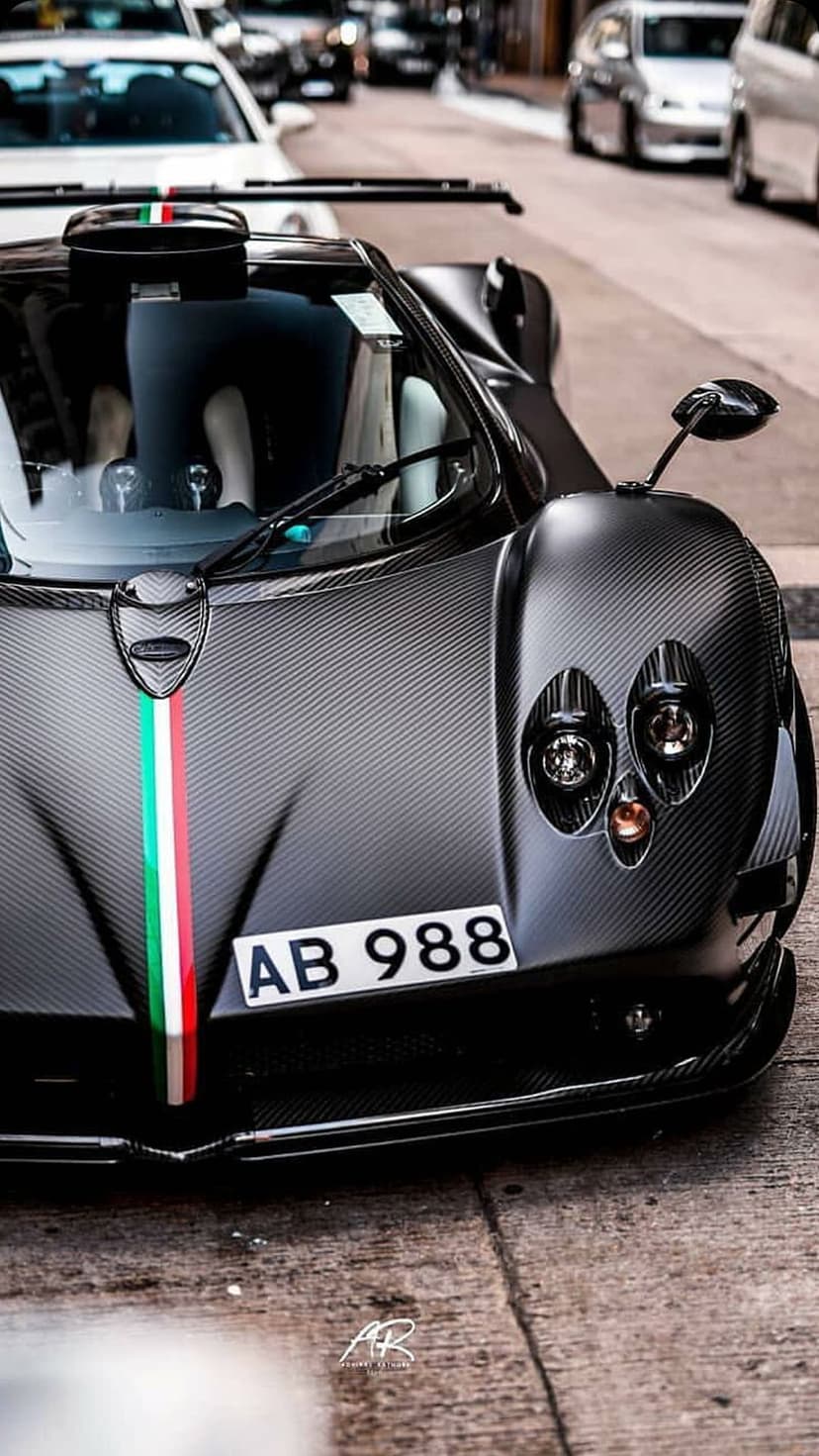 Frontal view of a carbon fiber sports car featuring an Italian flag stripe and glowing headlights on the hood.