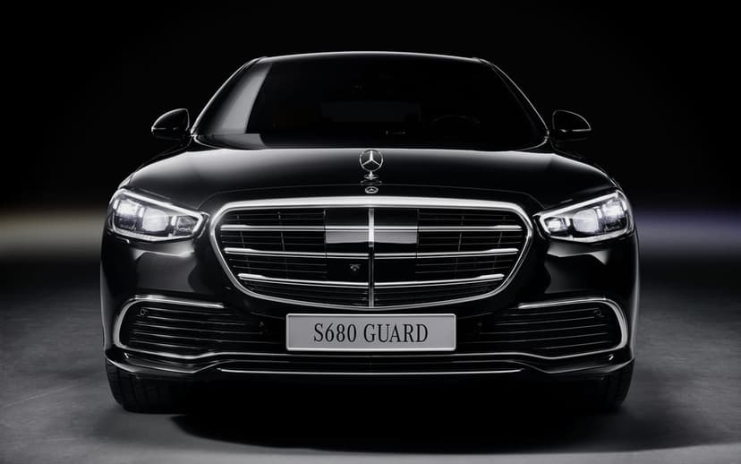 Black Mercedes-Benz S680 Guard front view with glowing LED headlights and chrome grille in a dark studio.