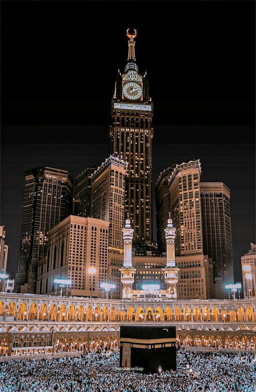 Abraj Al-Bait clock tower illuminates the night sky above the Kaaba and crowds in the Great Mosque courtyard.