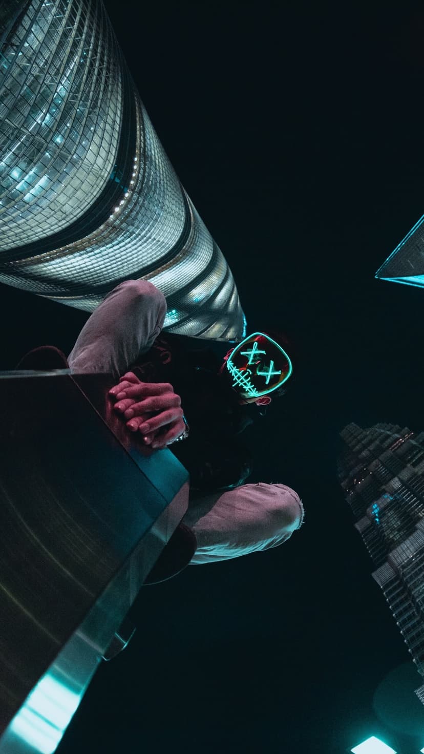 Masked figure with glowing green X eyes gazes down from high-rise skyscrapers against a dark urban night sky.
