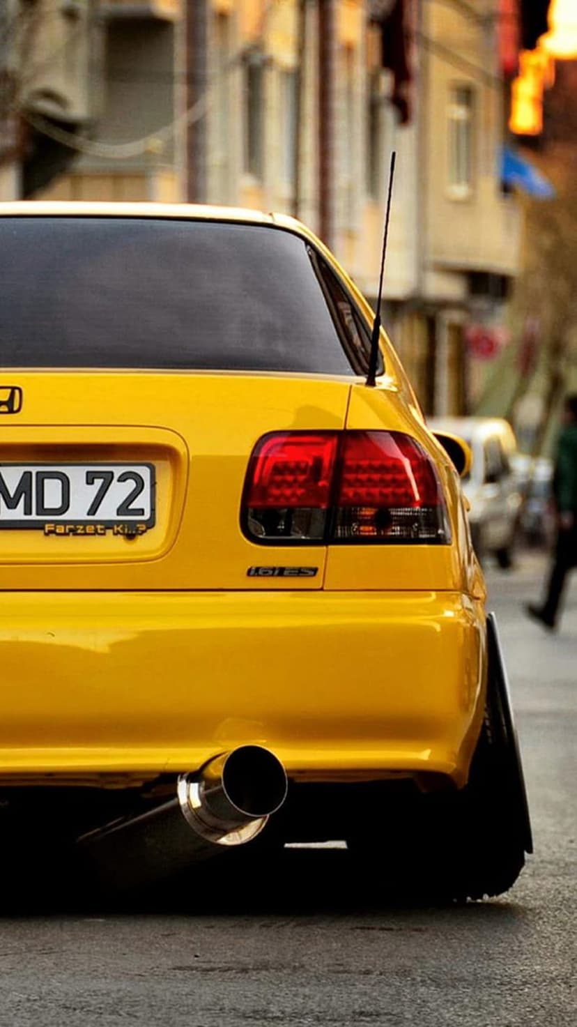 Yellow Honda Civic SI rear view with custom LED taillights and a polished exhaust pipe on an urban street.