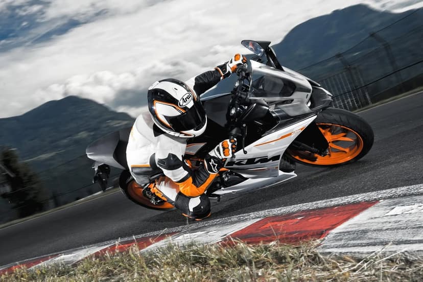 A KTM sportbike rider in white and orange gear leans deeply into a corner on a curved mountain racetrack.