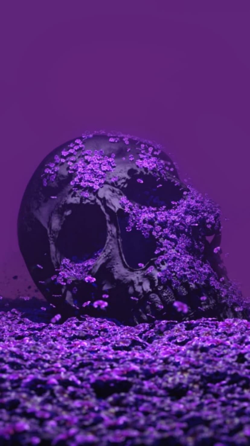 Human skull adorned with deep purple flowers and small pebbles, resting against a dark and moody backdrop.