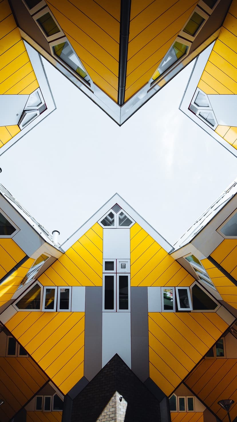 Yellow tilted cube houses viewed from below against a bright sky, highlighting sharp geometric architecture.