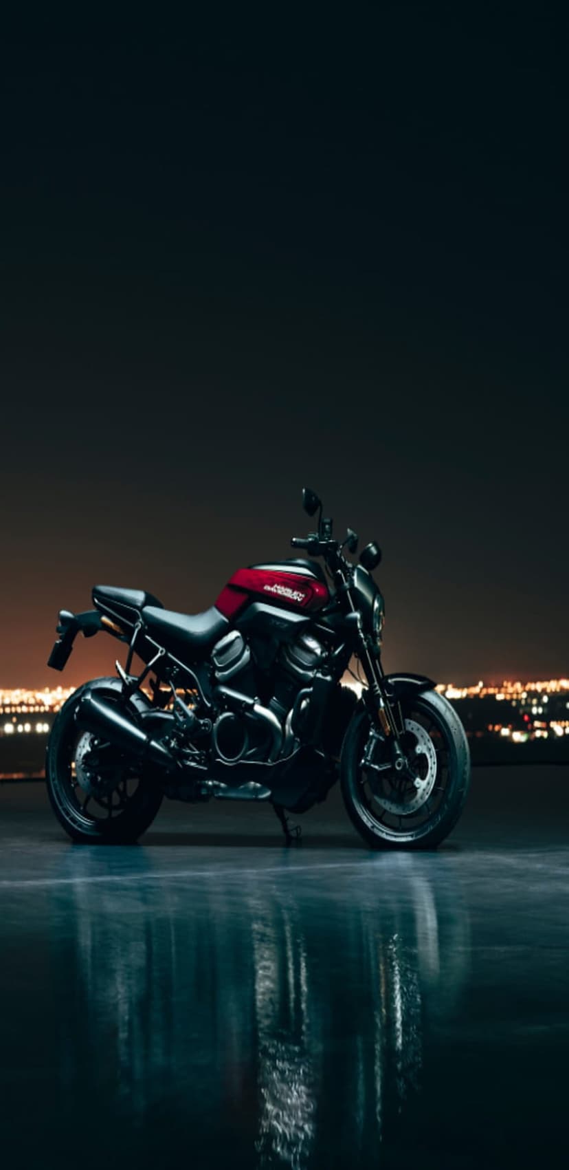 Harley-Davidson Sportster S motorcycle parked on a wet urban street at night with a distant city skyline bokeh.
